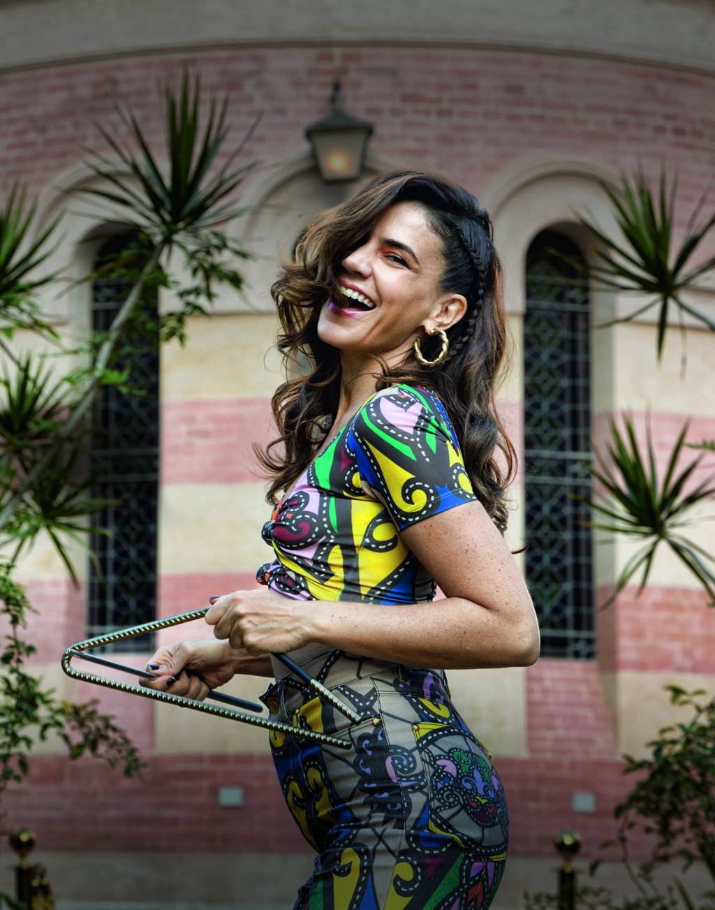 VEJASP-2792 Imagem mostra mulher de roupa colorida, sorrindo e tocando triângulo.