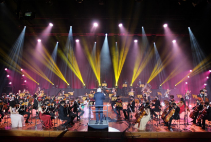 Imagem mostra orquestra se apresentando em palco colorido