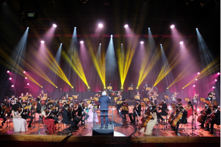 Imagem mostra orquestra se apresentando em palco colorido