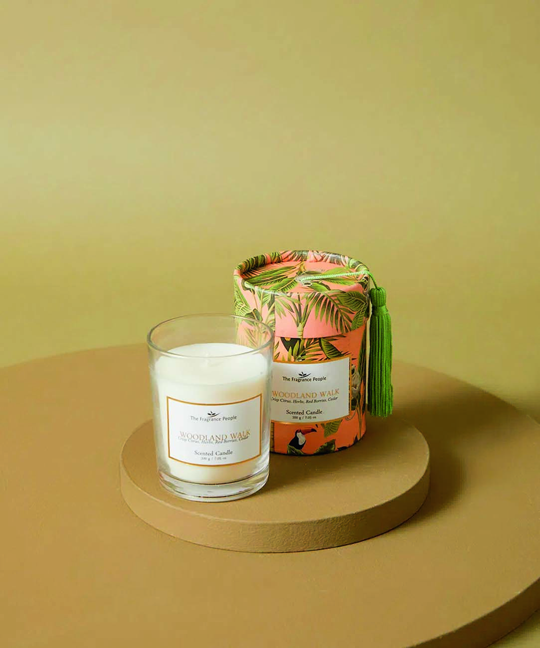 Vela aromatizada branca dentro de embalagem de vidro. A caixa, ao lado, &eacute; rosa e possui estampa de folhas verdes