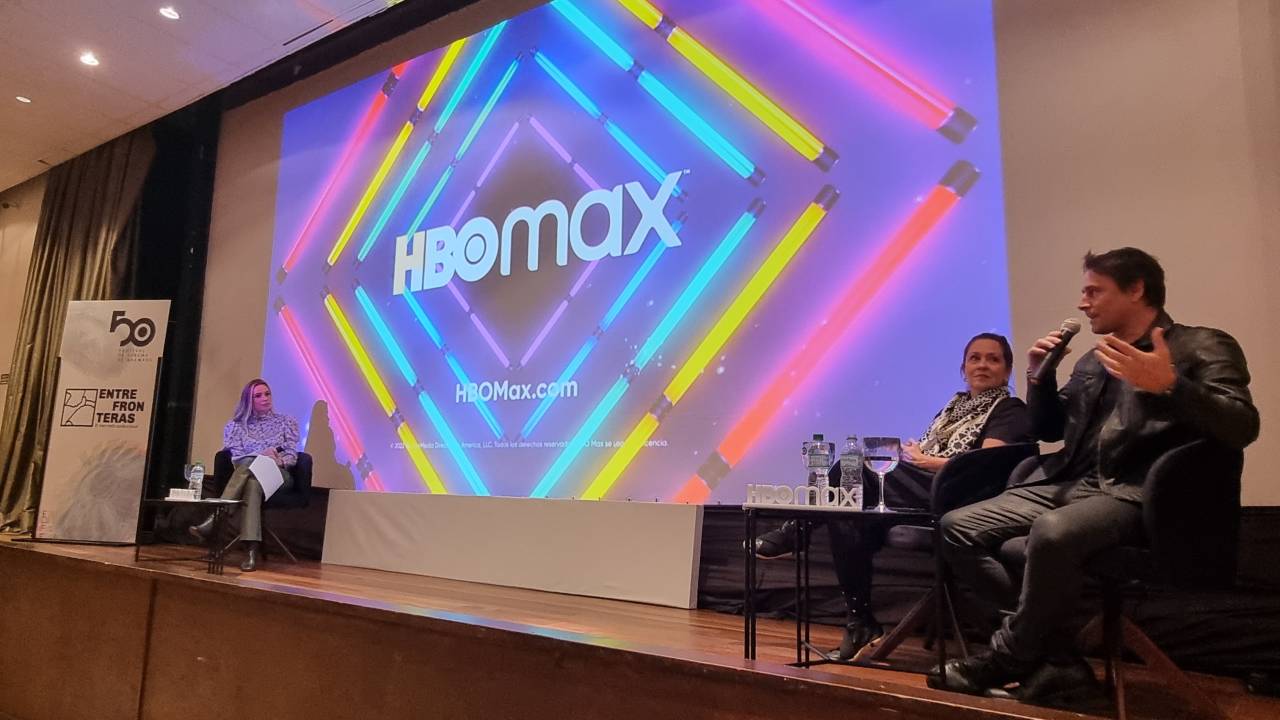 Registro da palestra da HBO Max; três participantes no palco, logo da marca na tela