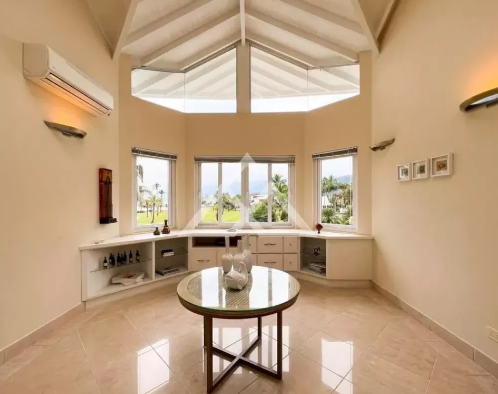 Casa é vendida a R$ 18 milhões (Divulgação) Foto exibe hall com pé-direito alto, janelas e mesa de centro.