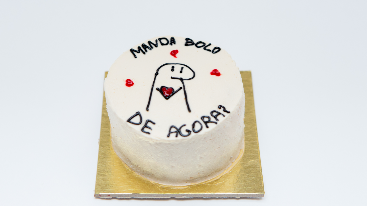 Bolo branco com a frase 'manda bolo de agora' e um personagem com corações ao redor.