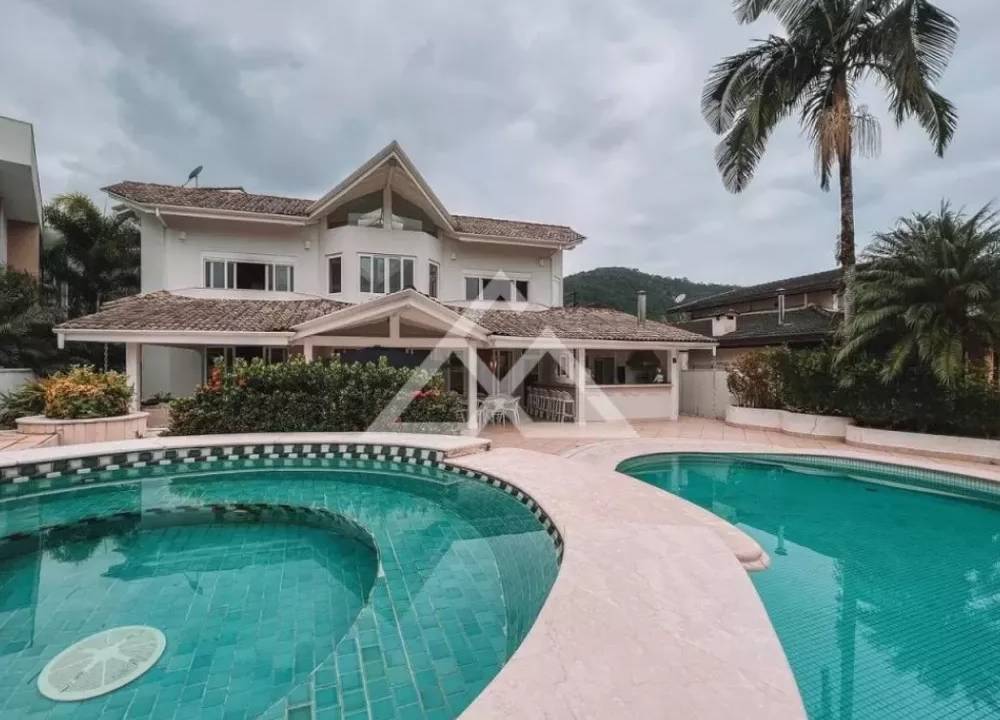 Foto exibe fachada de mansão com duas piscinas amplas na frente.