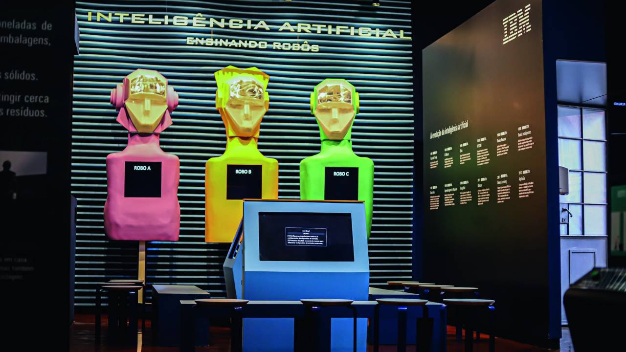 Imagem mostra sala com três robôs coloridos ao fundo