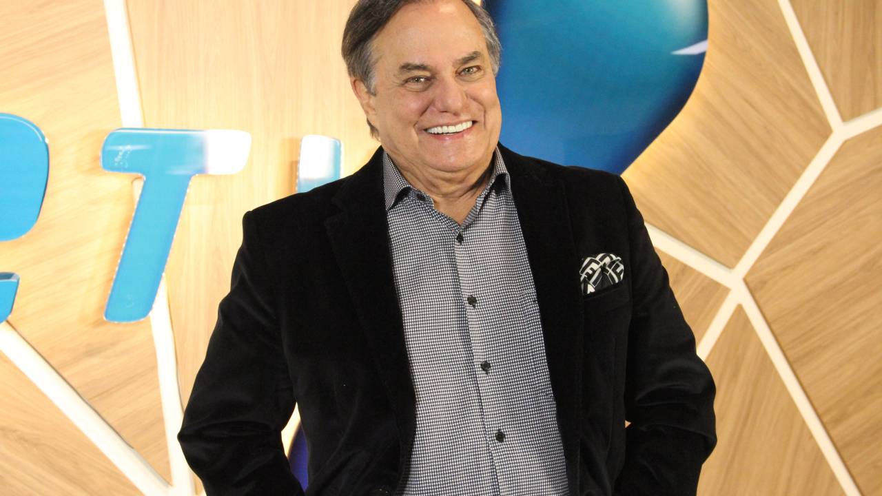 Ronnie Von sorri com camisa azul e paletó preto.
