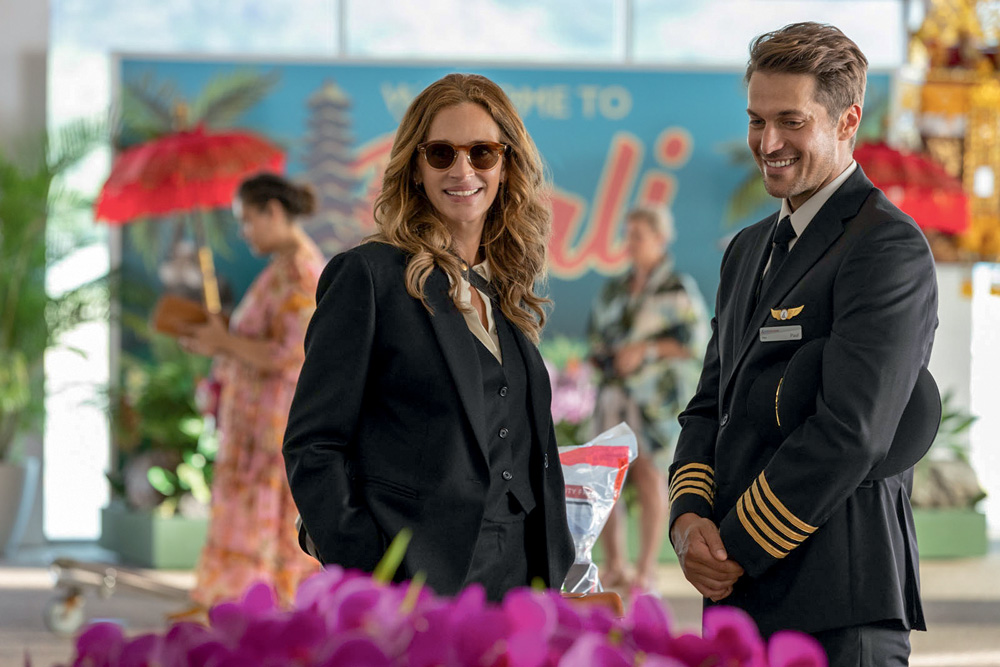 ingresso para o paraíso – credito Universal Studios 2.jpg Imagem mostra mulher de terno e óculos escuros rindo ao lado de homem com roupa de piloto de avião