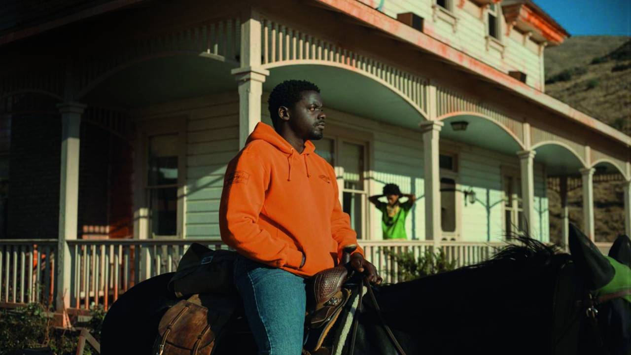 Imagem mostra homem vestindo casaco laranja e calça jeans em cima de cavalo