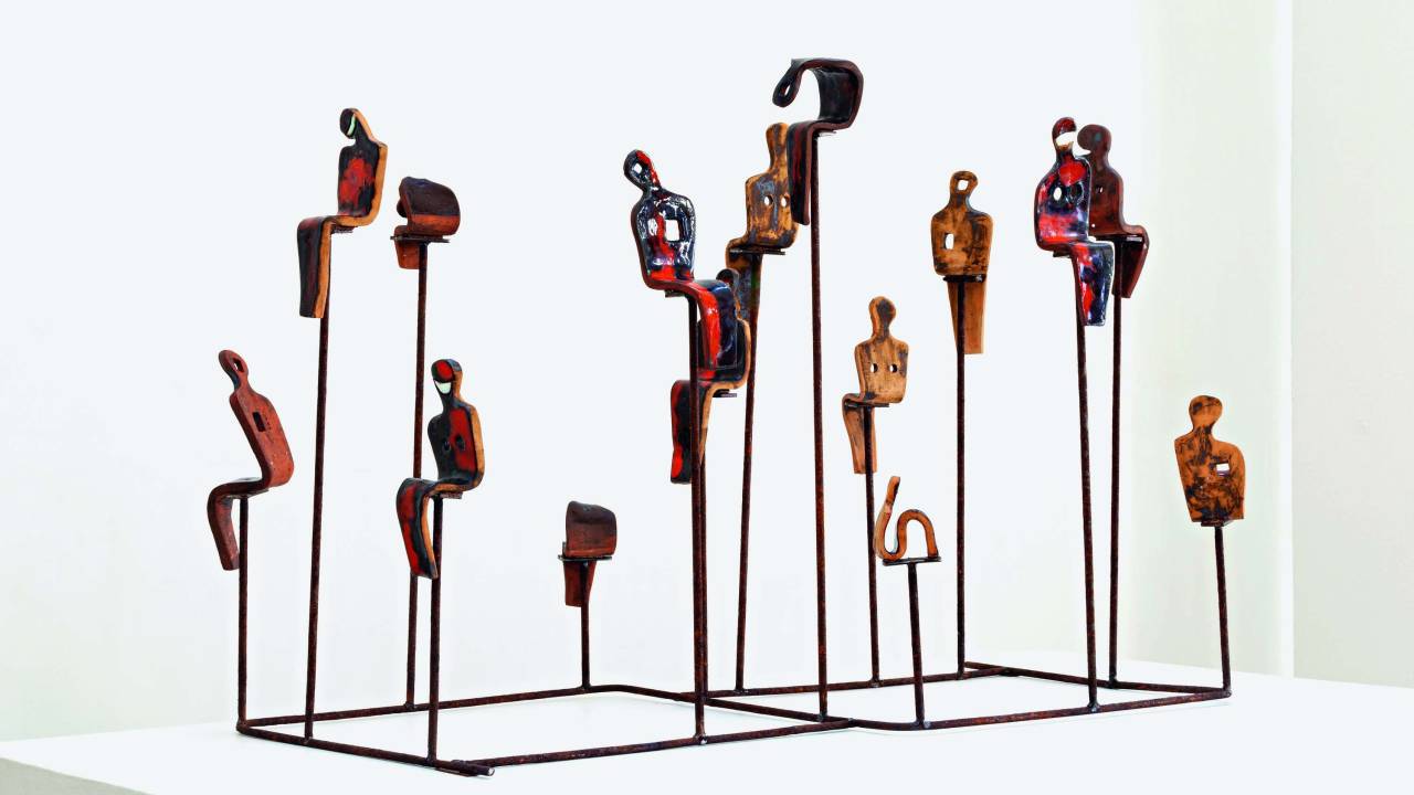 Obra feita de cerâmica tem figuras parecidas com seres humanos sentados elevados por arames. Esses arames e se juntam uns aos outros formando uma base quadrada, que é apoiada no chão
