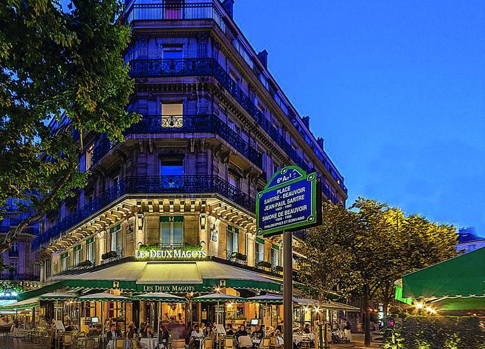 Fechada de prédio de esquina iluminado, com toldo verde cobrindo mesas externas
