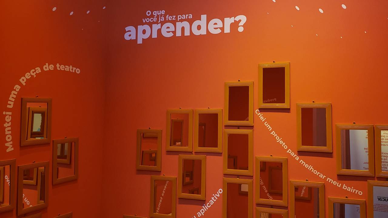 Parede repleta de espelhos com o texto "O que você faz para aprender?"