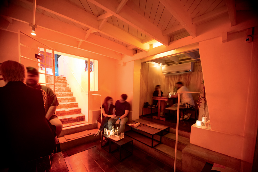 Salão do Cava Bar. Tem um escada que dá para um subsolo com vários casais sentados. A luminosidade é amarelada e aconchegante