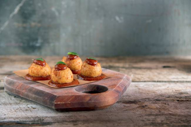 Tábua de madeira com petisco de bolinha de queijo com compota de tomate em cima