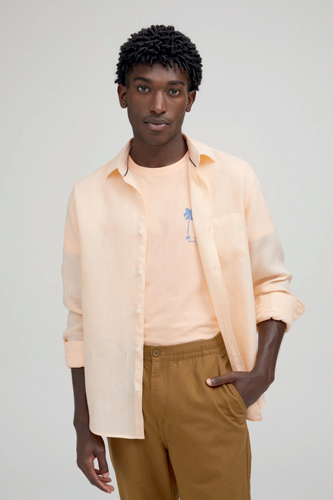 Modelo negro e magro usa camiseta rosa salm&atilde;o e, por cima, camisa da mesma cor com manga longa