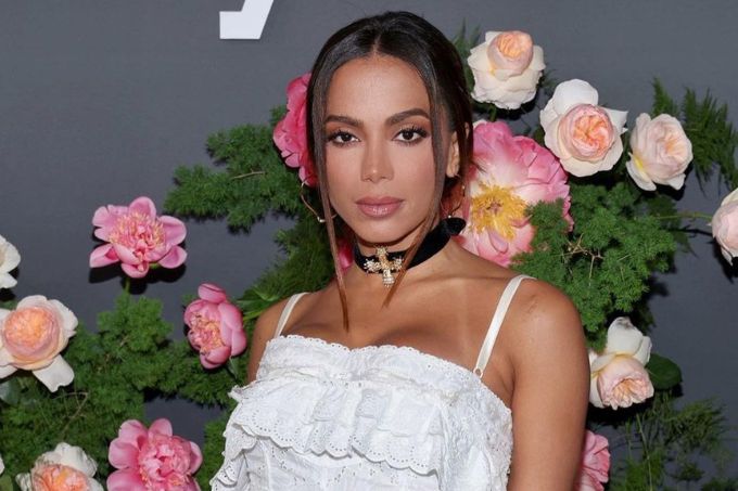 Foto mostra Anitta usando vestido branco, com semblante neutro, em fundo florido