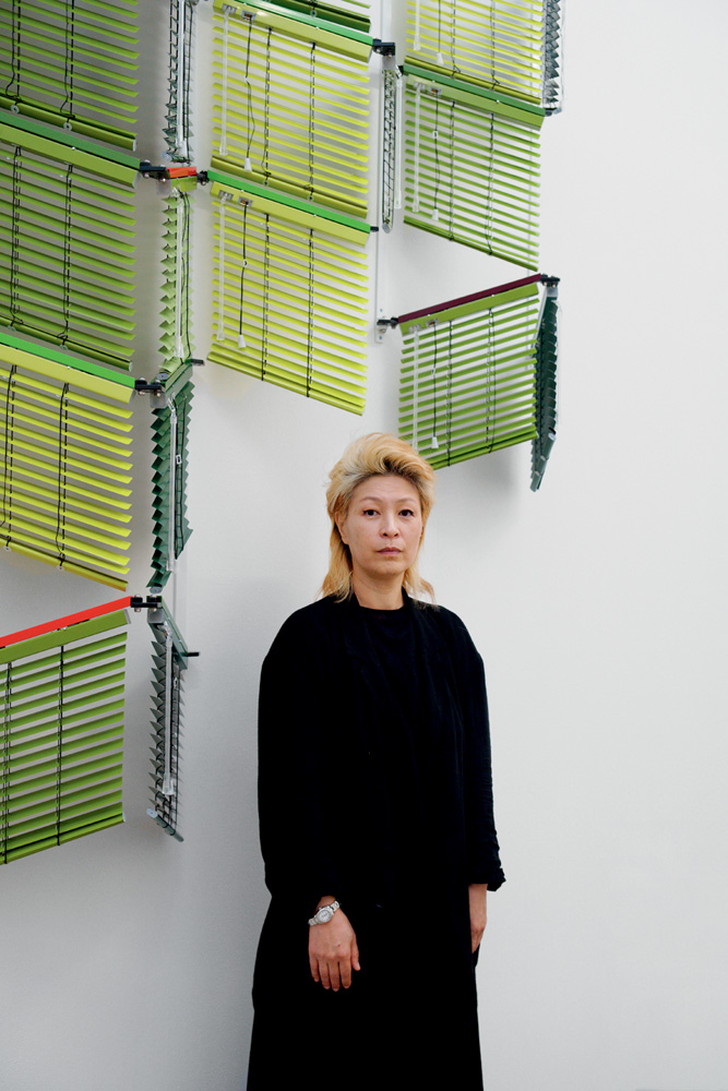 GCC 2022-Haegue Yang-portrait-004 Imagem mostra mulher de roupa preta em frente a parede branca