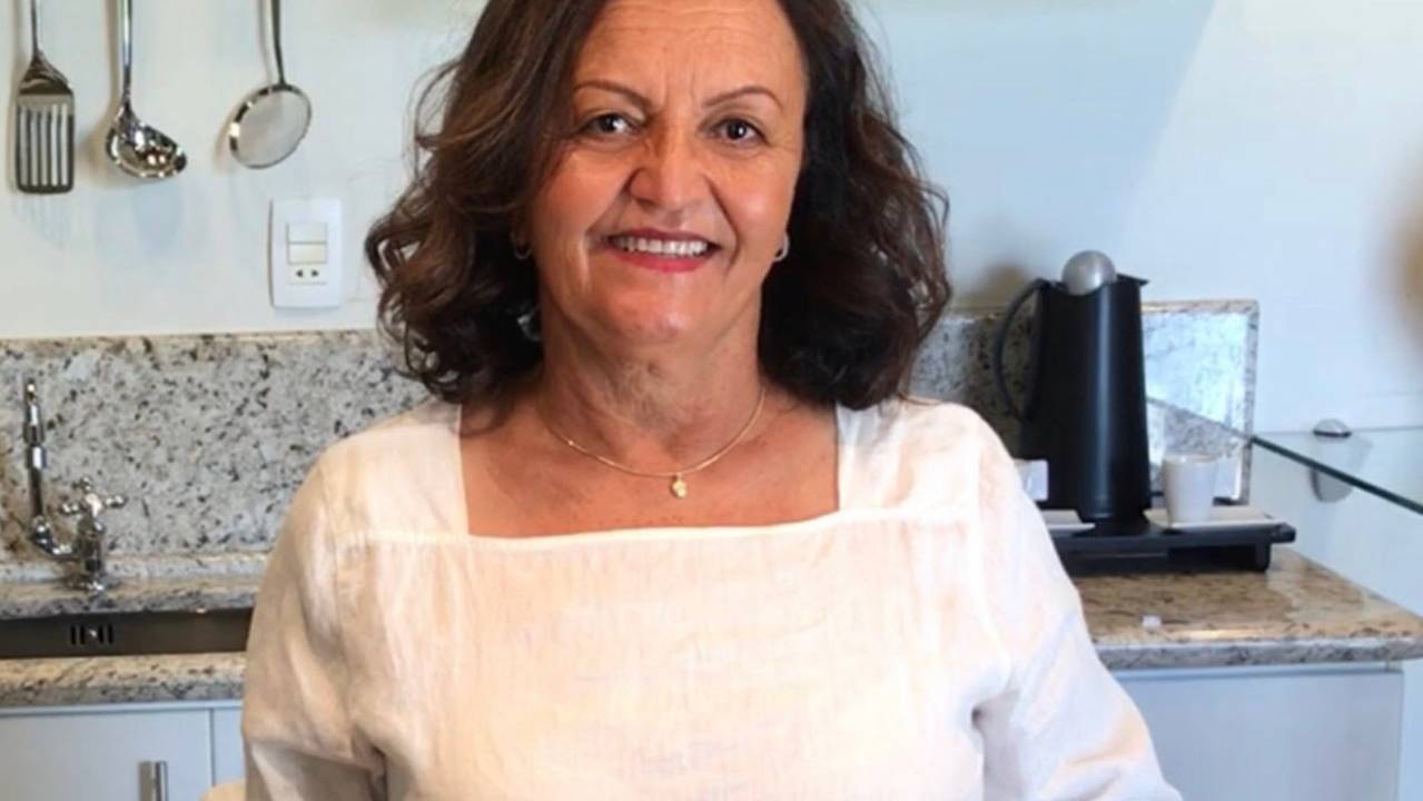 Foto de Eleni Moreti usando camisa branca, em uma cozinha, com utensílios ao fundo