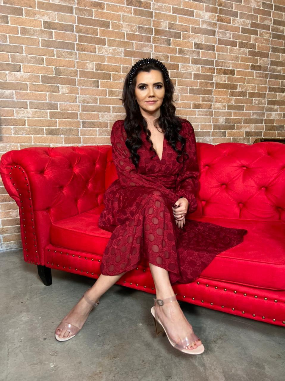Kélida (DMZP filmes e Fotos) (1) Espiritualista Kelida Marques posa sentada de pernas cruzadas em sofá vermelho. Veste vestido também vermelho e tem cabelos pretos longos.