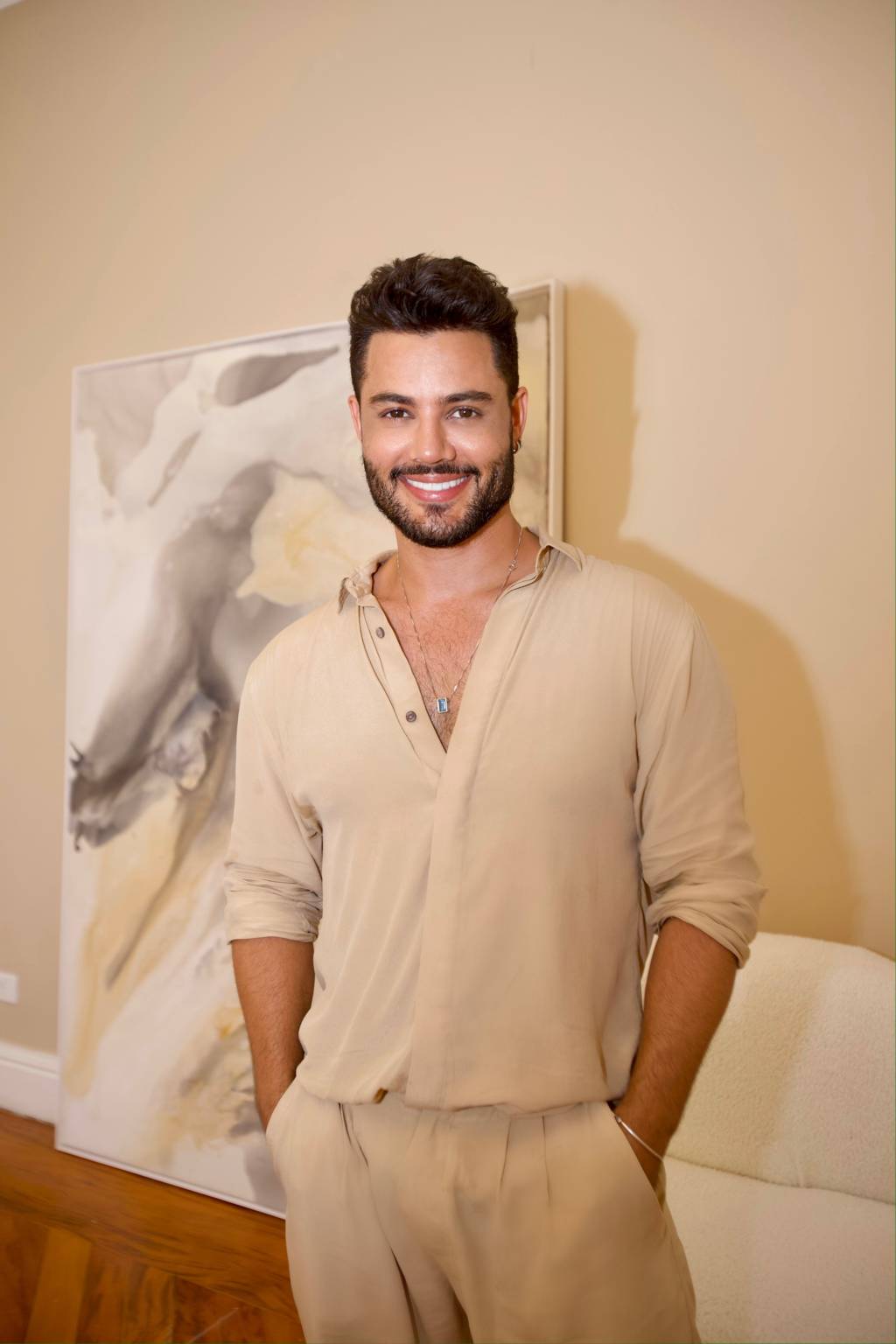 Well Dias (Caco Andrade-Divulgação) Hair stylist Well Dias sorri para a câmera. veste blusa bege com botões abertos, tem cabelos pretos e barba.