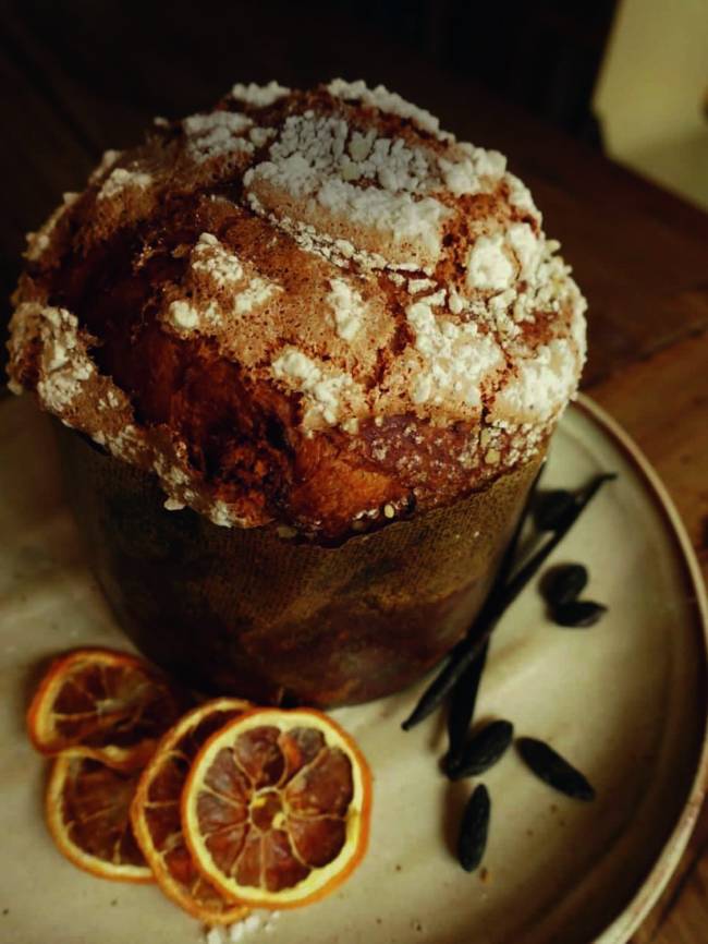 Mocotó Panetone Panetone inteiro sobre prato onde há fatias de laranja desidratada