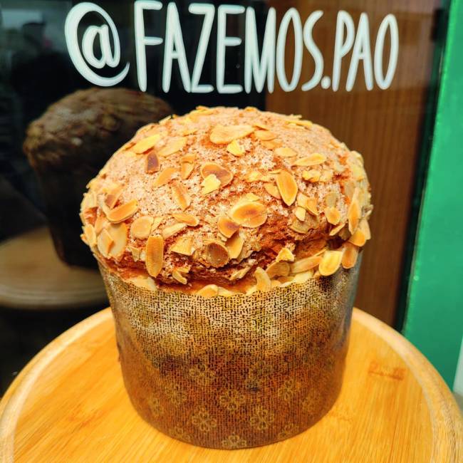 Panetone sobre mesa redonda de madeira clara com amêndoas açucaradas na casca