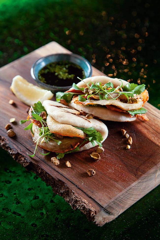 bao porchetta Basilicata Tábua de madeira com dois baos e um pote de alumínio com molho e uma fatia de limão em forma de cunha
