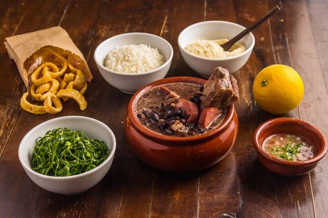 Feijoada com cada um dos ingredientes/pratos separados em uma cumbuca