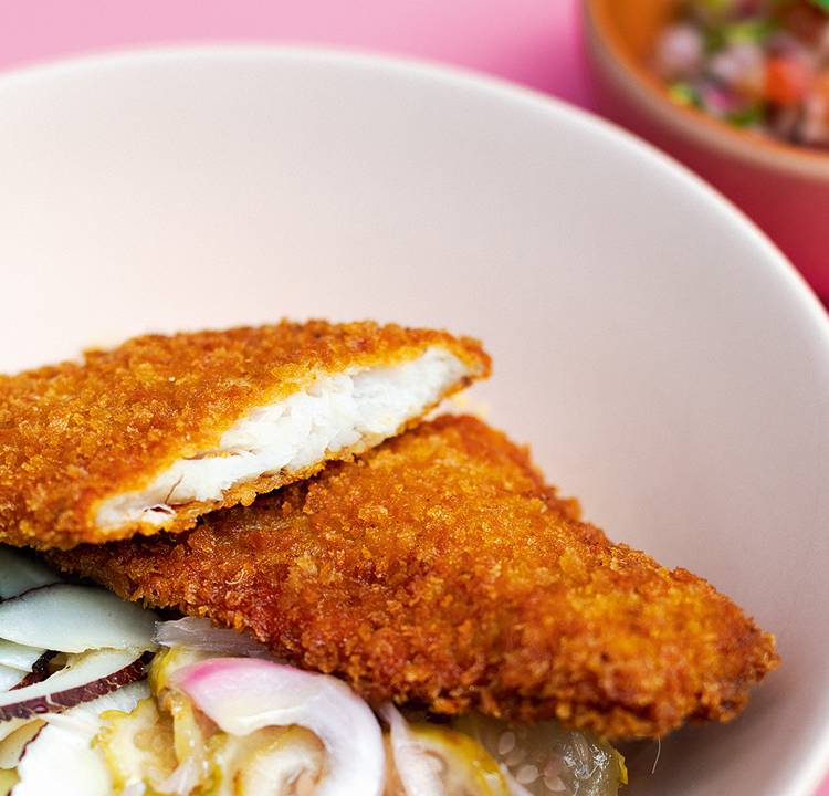 Prato contendo peixe frito e picles de vegetais sobre mesa cor de rosa