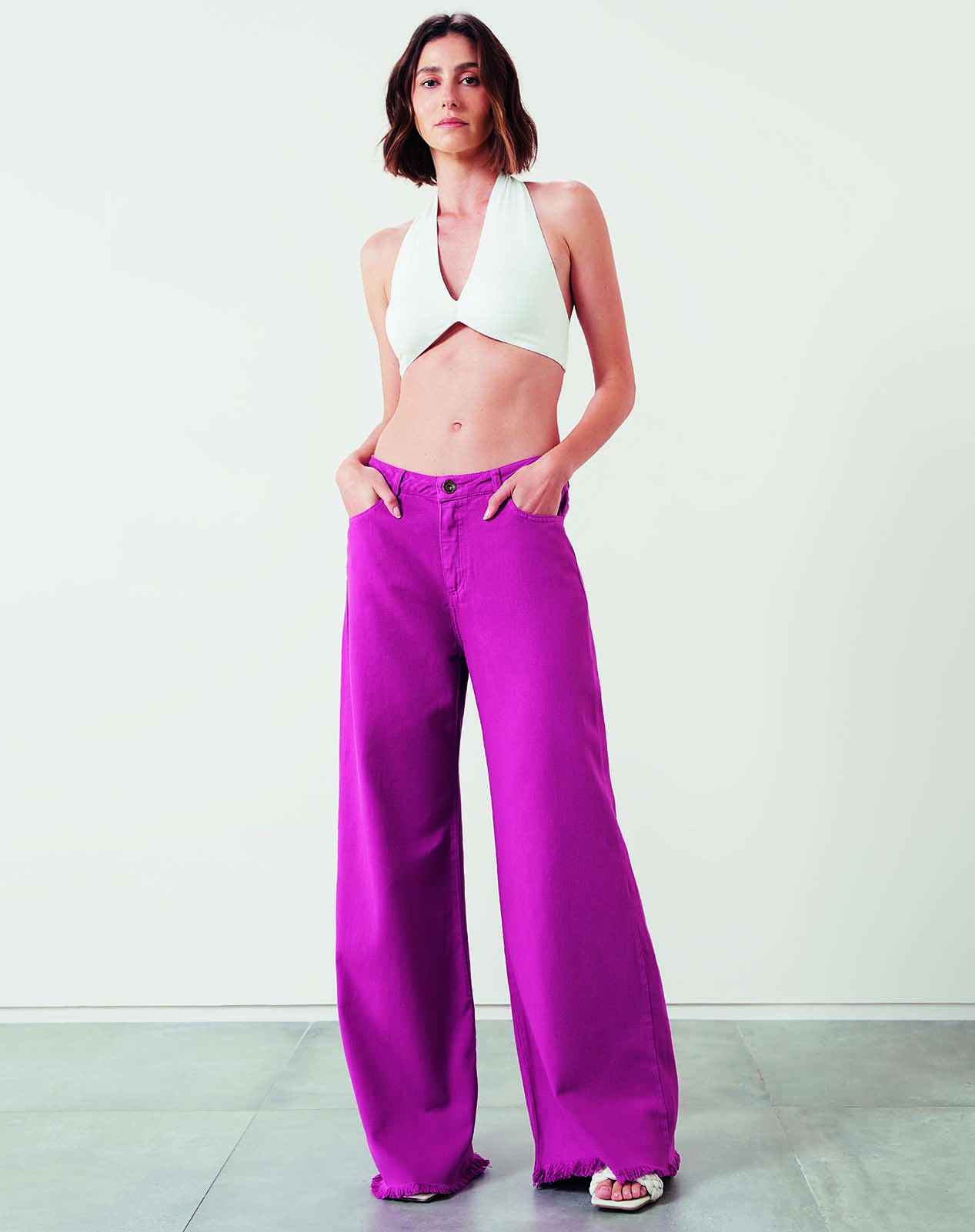 Modelo branca, magra, de cabelos curtos, lisos e escuros usa cropped branco e cal&ccedil;a jeans magenta