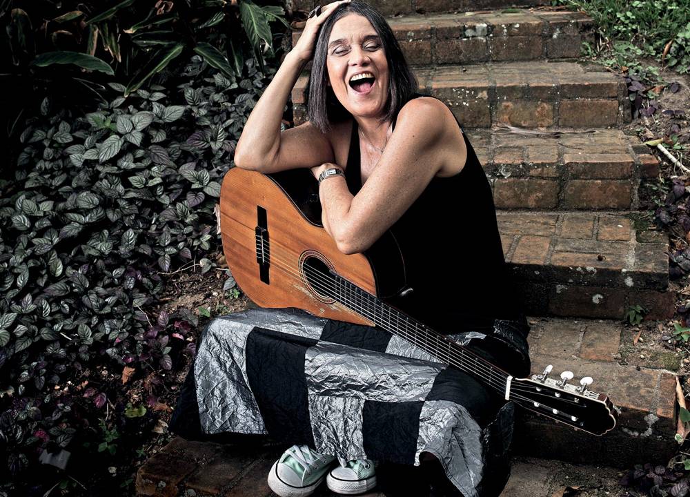 Imagem mostra mulher sorrindo, segurando violão no colo