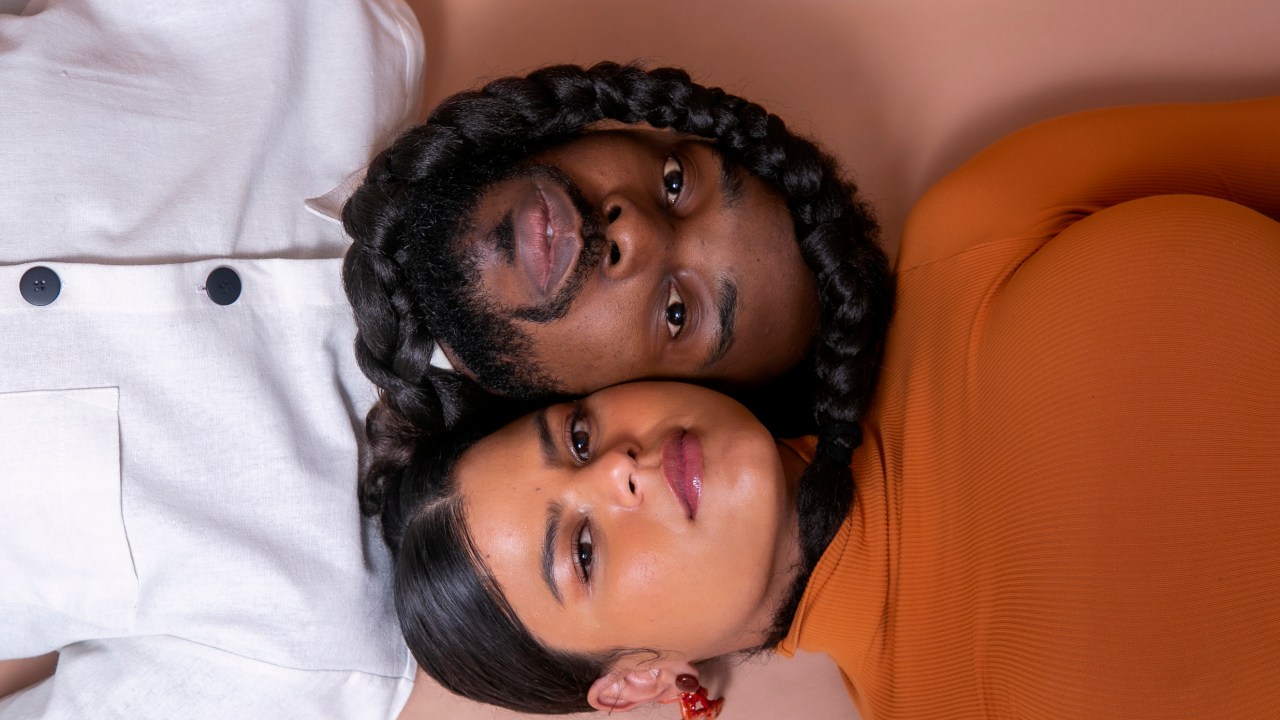 Imagem mostra homem e mulher deitados, com cabelo da mulher trançado enrolado no rosto do homem