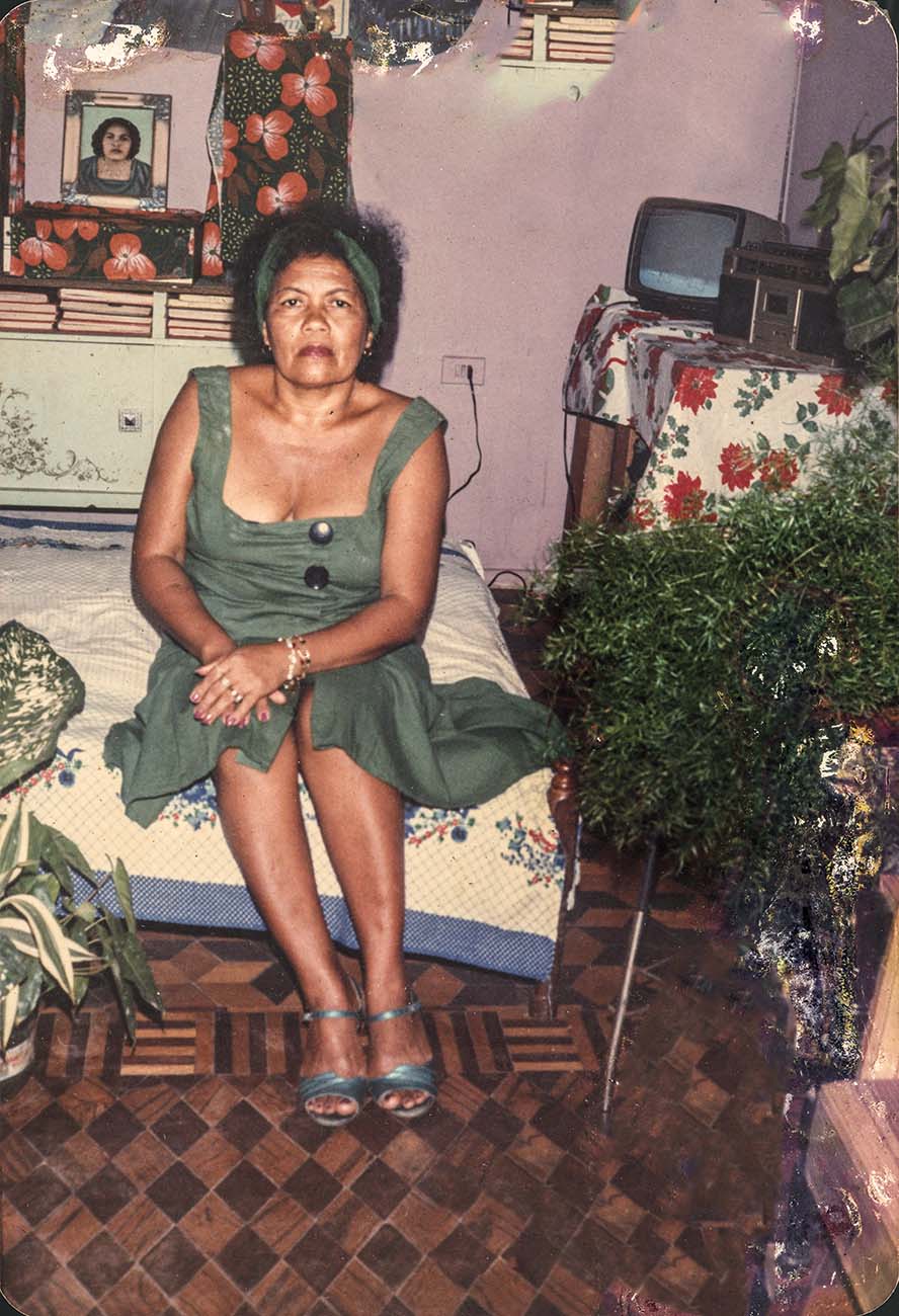 Dona Onete Imagem mostra mulher sentada em cama, dentro de quarto