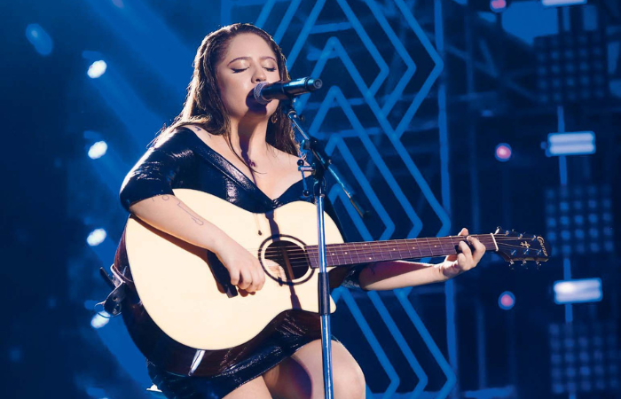 Imagem mostra mulher tocando violão em palco