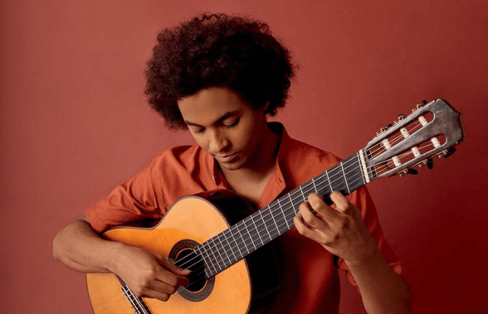 Imagem msotra homem segurando violão, com camisa vermelha