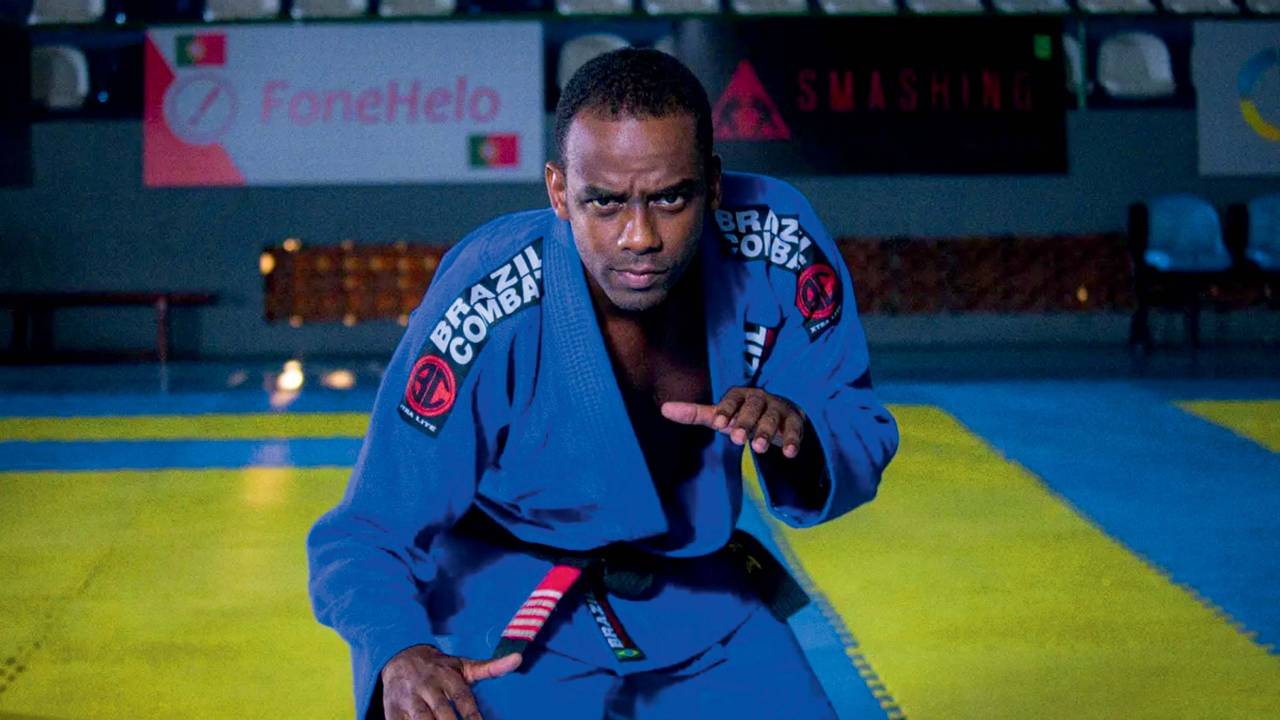 Imagem mostra lutador de jiu-jítsu com kimono azul, em posição de defesa