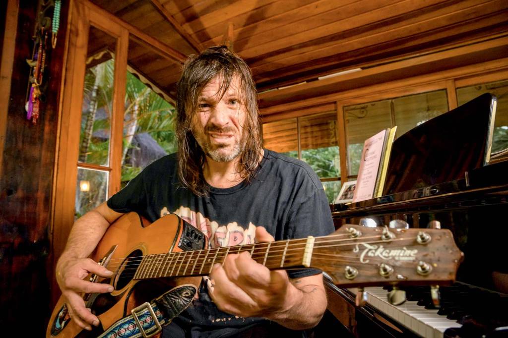 Evan Dando Imagem mostra homem de cabelos molhados, tocando violão em frente a piano e fazendo careta