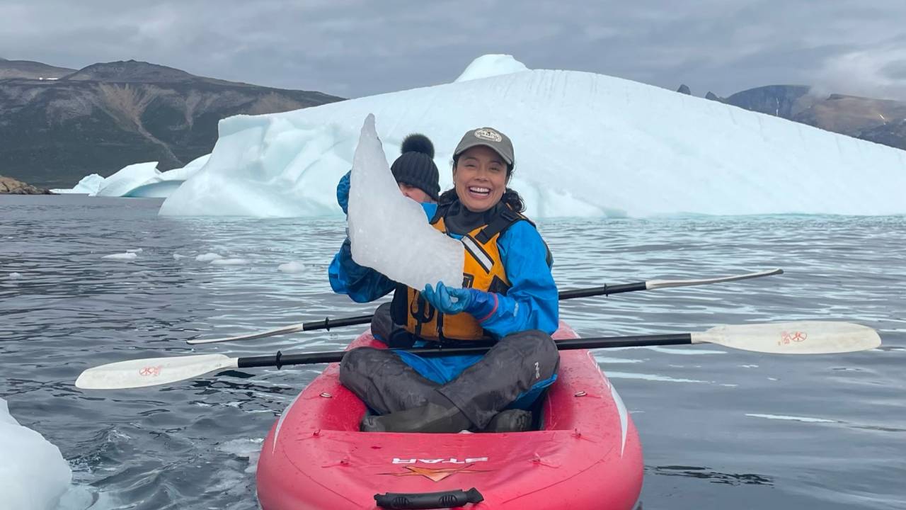 Daniela dentro de um barquinho vermelho e segurando uma placa de gelo em alto mar
