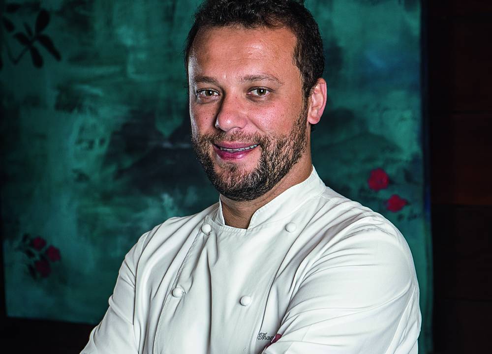Chef usa dolma branca e sorri para foto com os braços cruzados