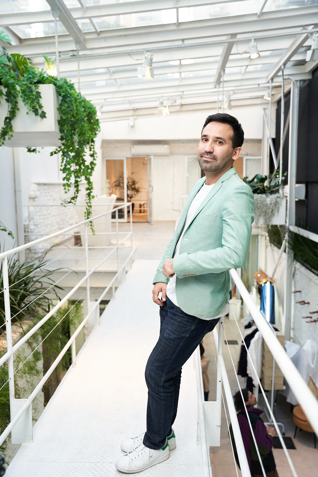 Homem branco posa apoiado em corrim&atilde;o. Veste jeans com blazer azul-beb&ecirc;.