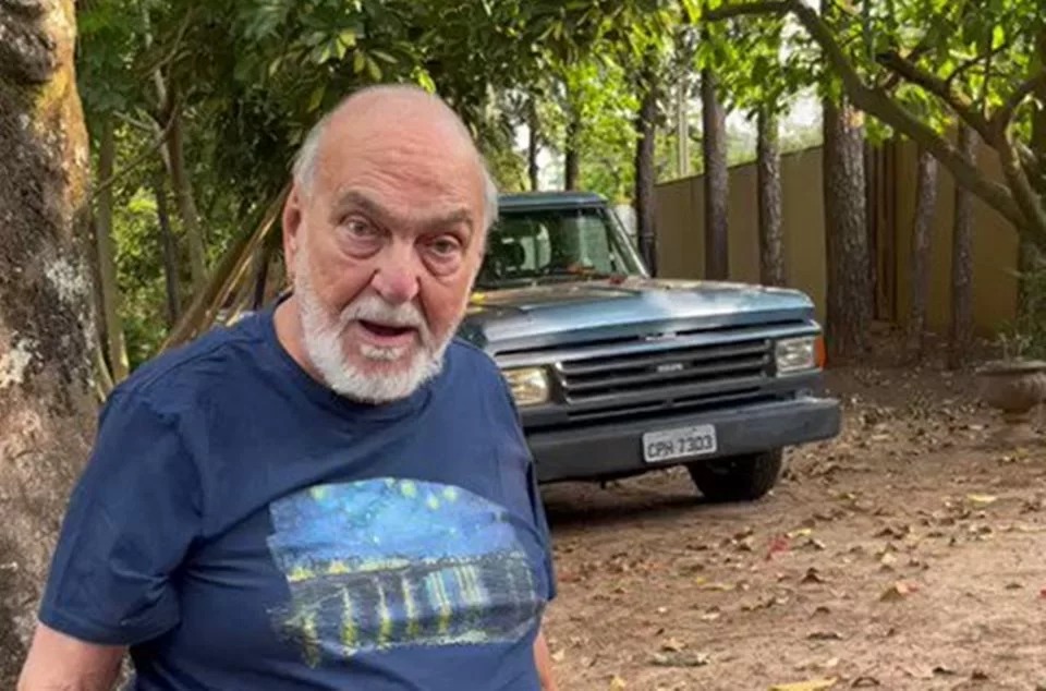 Lima Duarte posa com a boca aberta diante de carro antigo, em meio a paisagem florestal