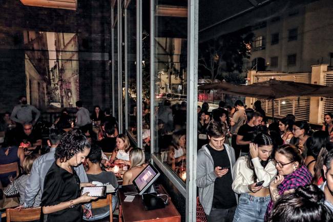 Ambiente interno de restaurante cheio com fila de espera do lado de fora da parede de vidro