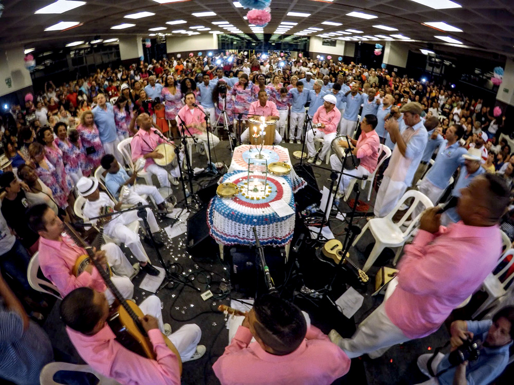 Samba da Vela Imagem mostra roda de samba com sambistas vestindo camisa rosa