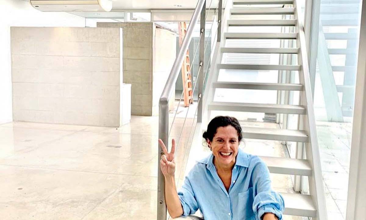 Mulher de camisa branca e calça clara sentada em escada