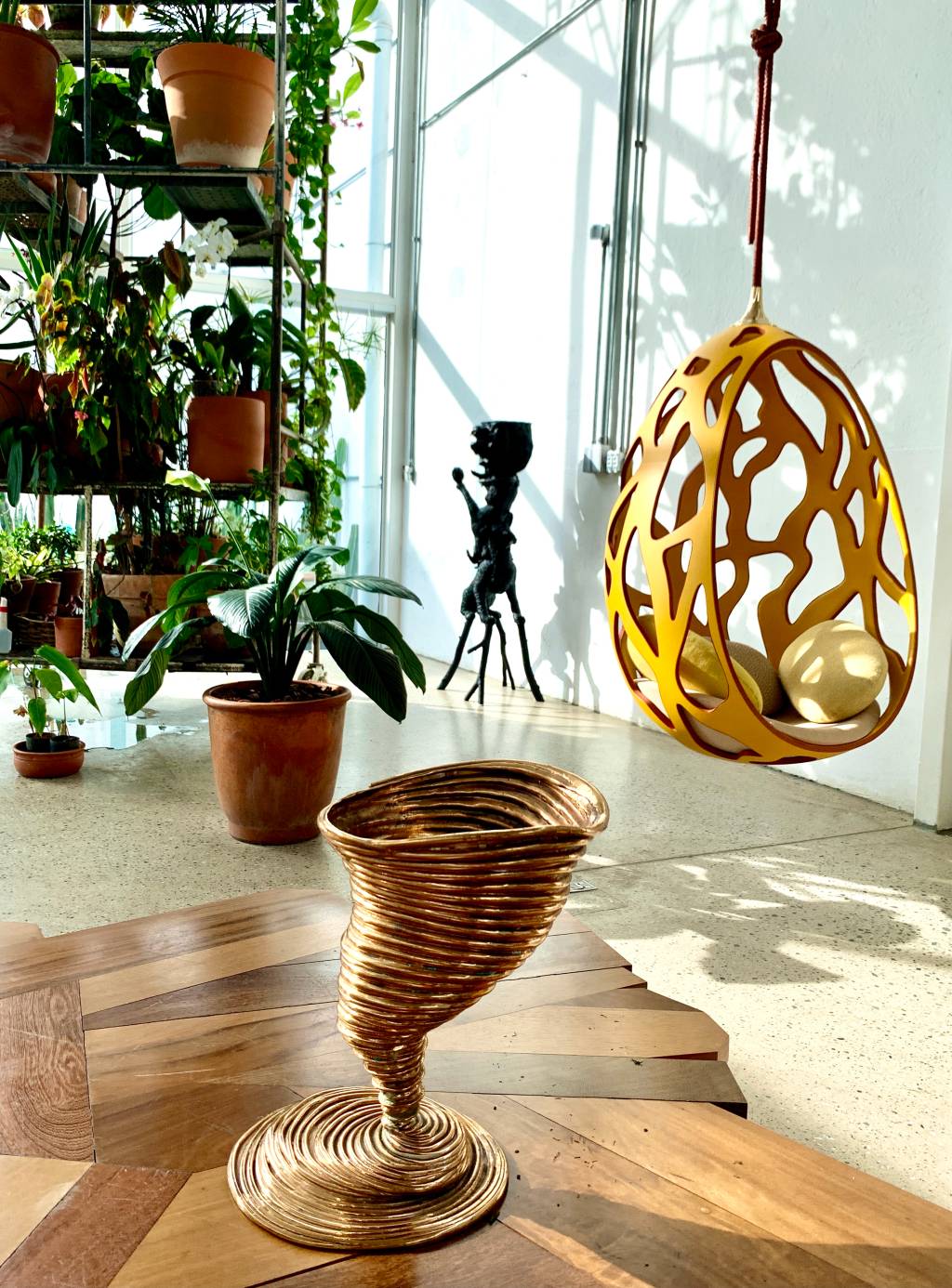 Estúdio_Campana_2023_Tornado_Cocoon_SL Vaso em formato de tornado e poltrona amarela suspensa em ambiente iluminado e com plantas.