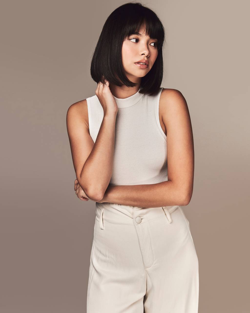 Yuki Sugimoto (Another Agency-Divulgação) Mulher oriental com cabelos pretos curtos posa olhando para a direita. Uma das mãos está próxima ao queixo. Ela veste regata e calça brancas.
