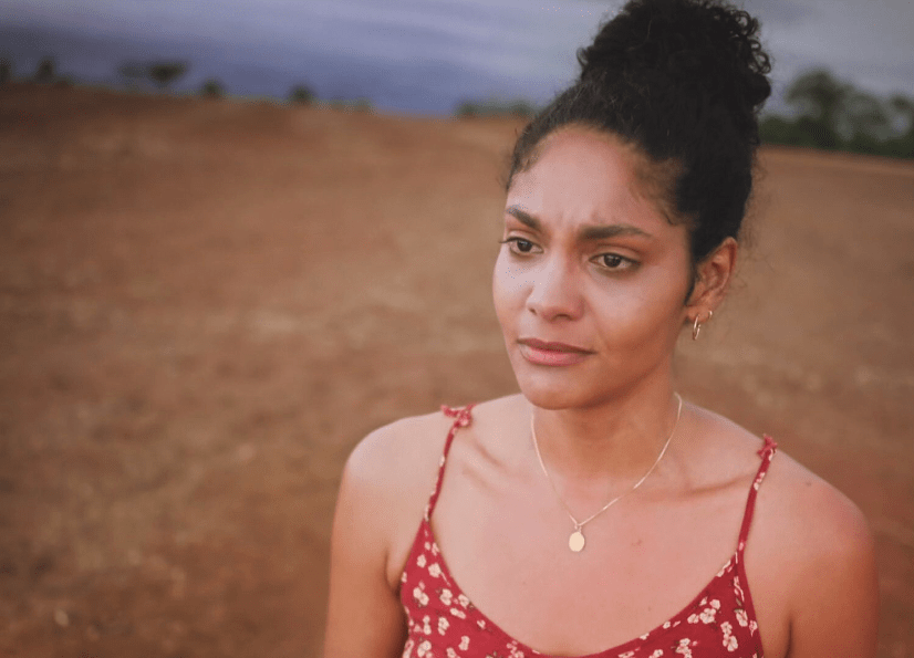 Uma mulher de cabelo preso e uma fazenda ao fundo