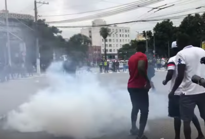 Homens se movimentam entre uma fumaça emitida por bomba de gás