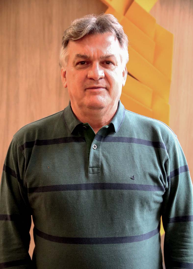 Eduardo Tambor, Diretor de Operações do Colégio Bandeirantes (Ricardo Birrer-Divulgação).jpeg Homem grisalho de camiseta com listras azuis e fundo verde escuro posa para a câmera.