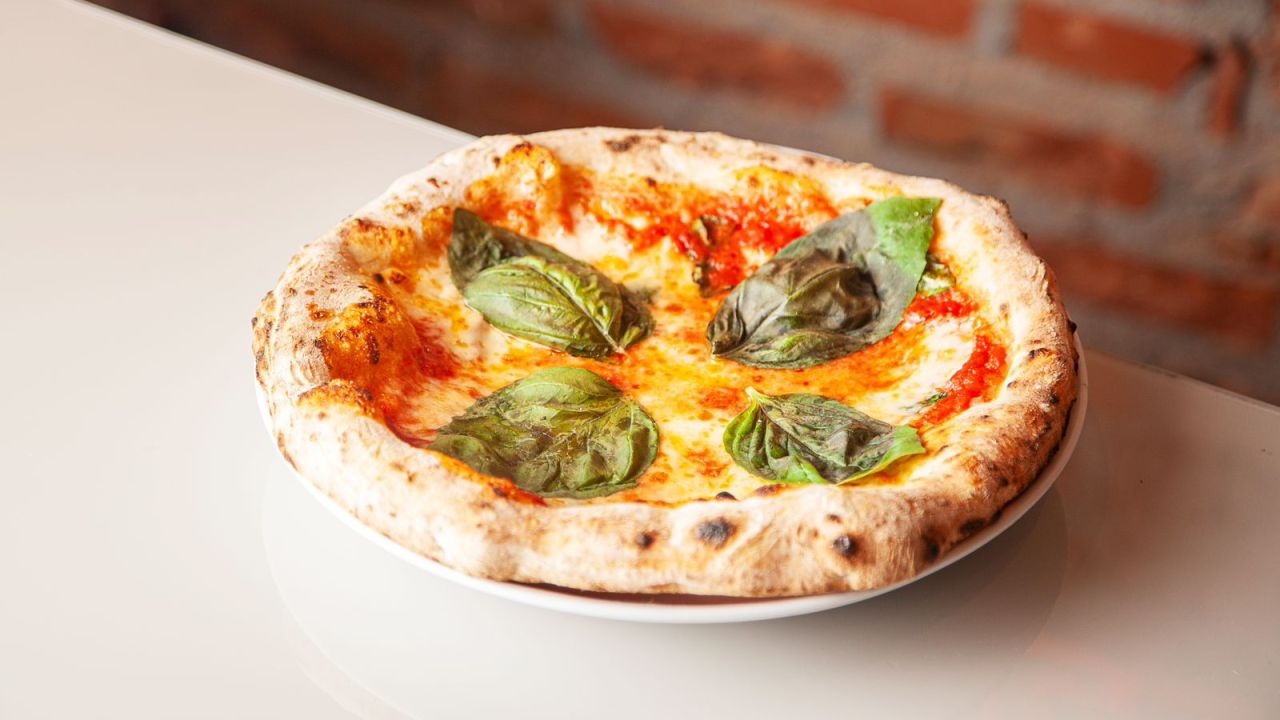 Pizza individual margherita em cima de bancada branca.