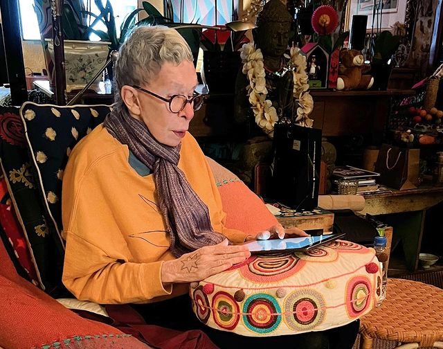 uma mulher de cabelos curtos e grisalhos sentada numa poltrona lendo no Ipad